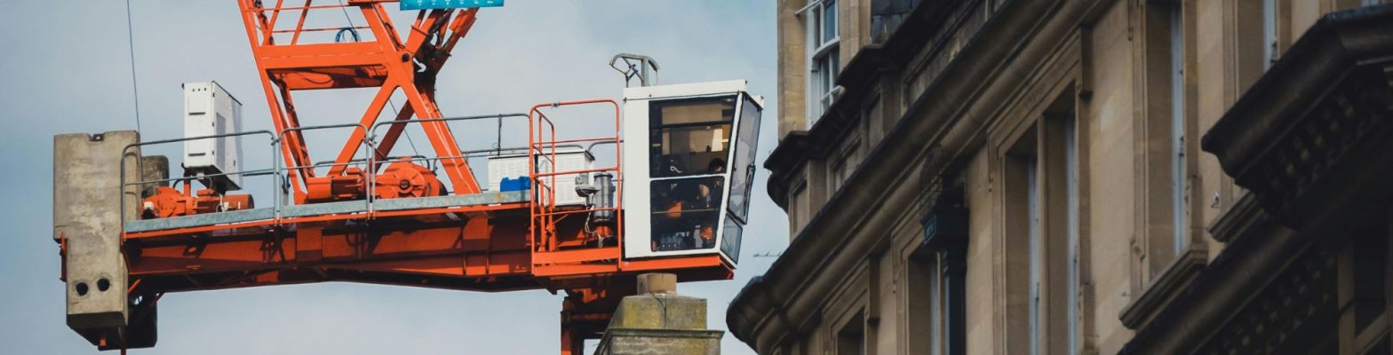 A red construction crane near a historic stone building, representing the Construction Industry Scheme (CIS) and tax compliance challenges for contractors and subcontractors in the UK. Photo by Zekai Zhu