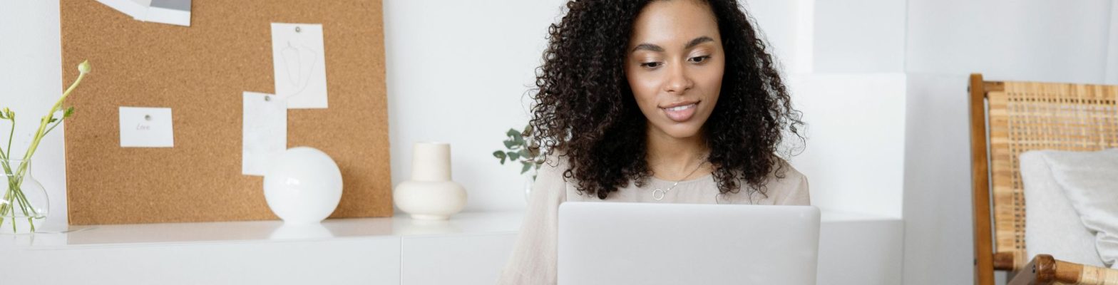 A young woman with curly hair, wearing a light-coloured blouse, sits in a calm, minimalist office space, working on a laptop with a relaxed and focused expression—representing mindfulness in financial management for small business owners.