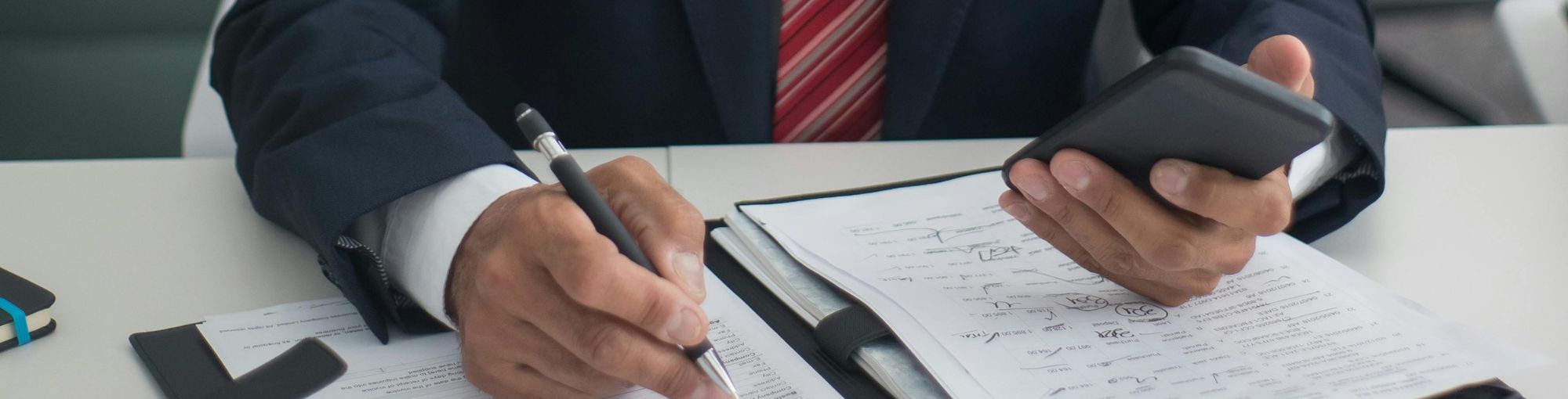 Senior finance professional in a suit reviewing business strategy and financial documents with a pen and smartphone in hand, representing Coopers&Co’s YourFD fractional finance director support for UK SMEs.